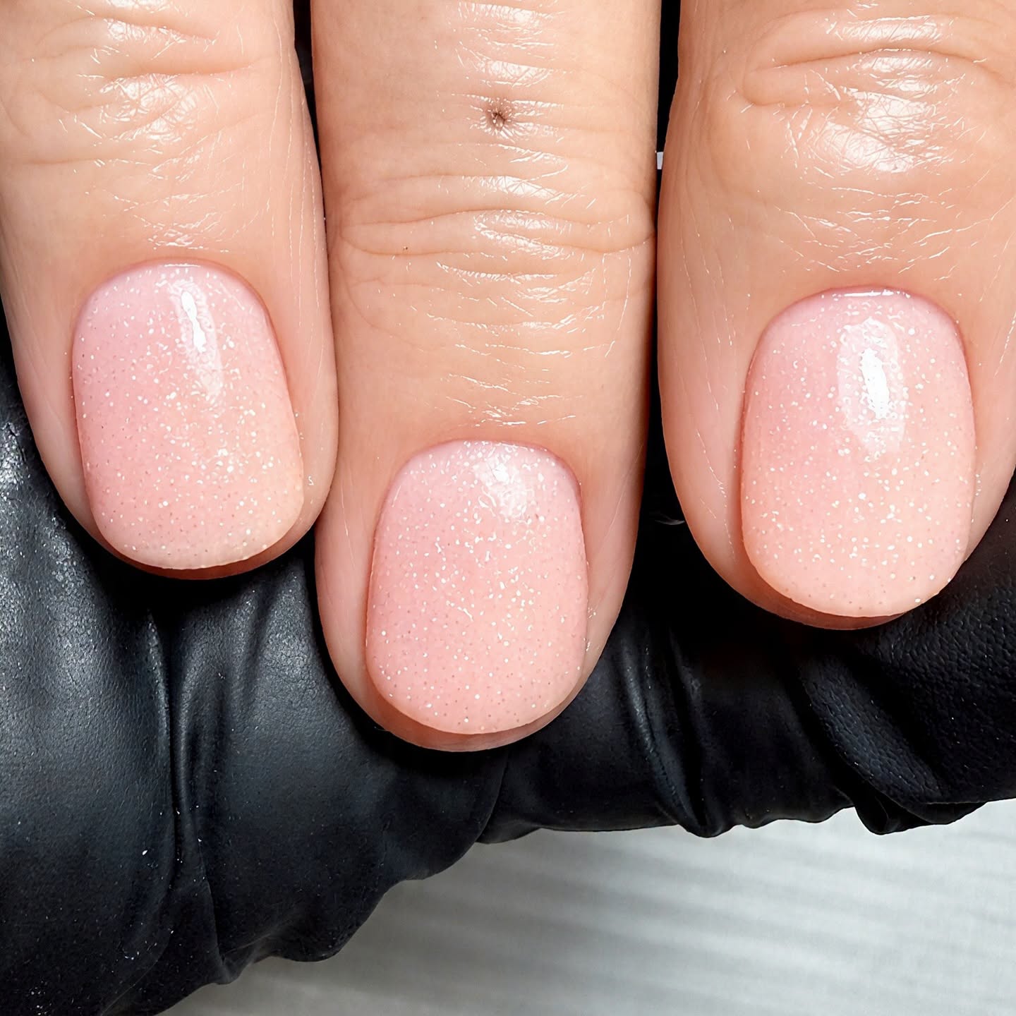 Close up of three manicured nails with pink glitter polish